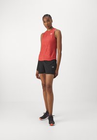 Red sleeveless athletic top with subtle pattern, paired with black shorts and black athletic shoes featuring orange accents.