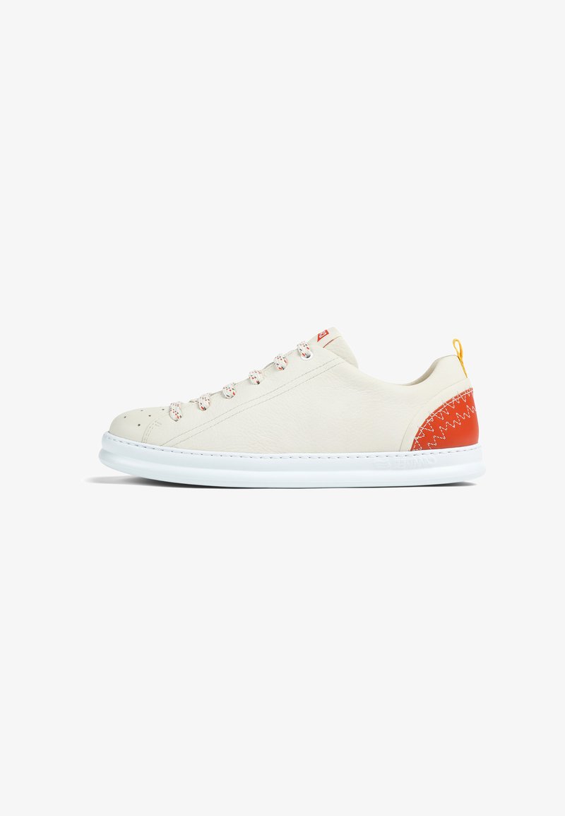 Zapatilla blanca de corte bajo con punta redondeada, cordones blancos con motas rojas, parche rojo en el talón con costura en zigzag y suela blanca.