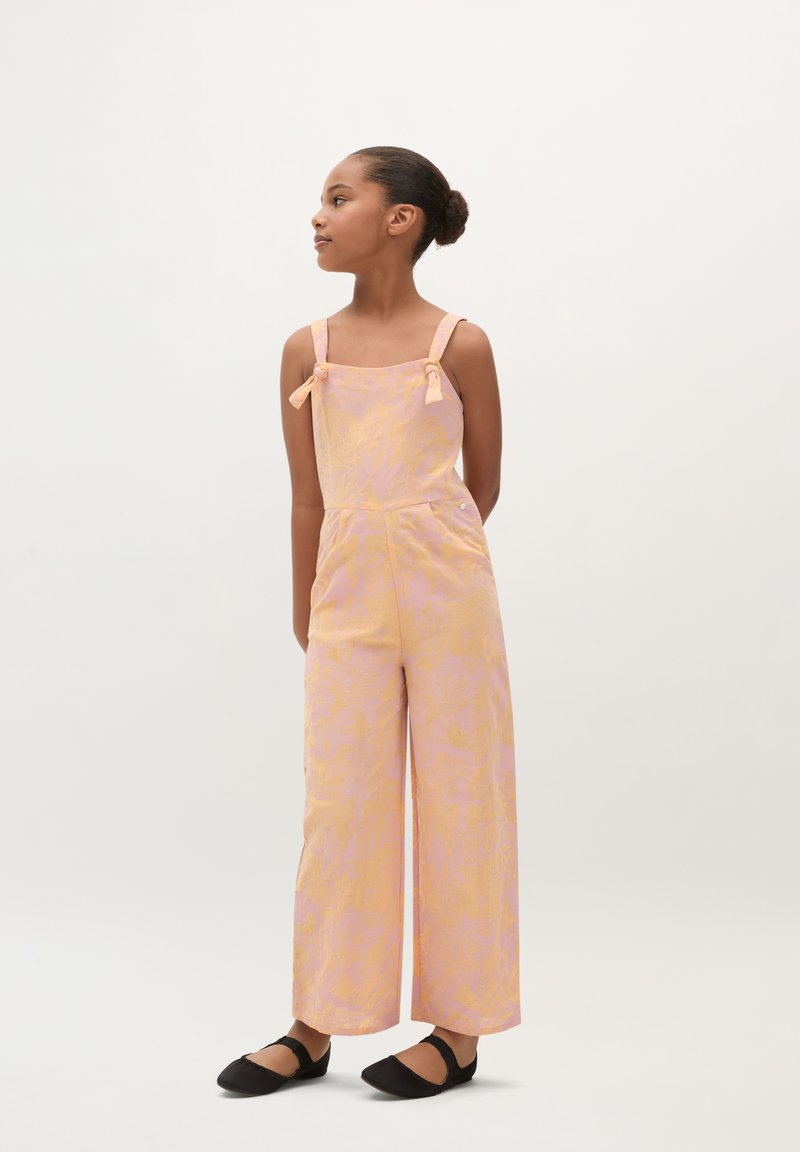 Letvægtigt jumpsuit i pink og orange med mønster, brede ben, justerbare stropper og afslappet pasform. Sammen med sorte flade sko.