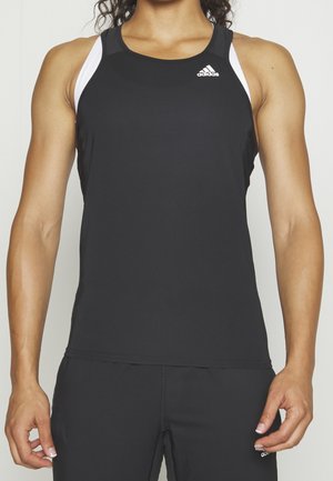 Woman wearing a black sleeveless Adidas sports top and matching black pants, standing with arms relaxed by her sides.