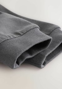 Szare bawełniane mankiety bluzy z prążkowaną teksturą. Charakteryzują się gładkim wykończeniem z lekkim postrzępieniem na krawędziach, ułożone starannie w stos.