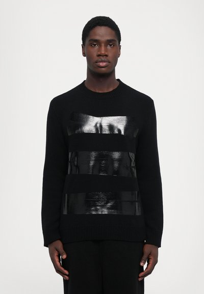 Maglione nero con un pannello testurizzato e lucido nero sul petto, colletto classico a girocollo e polsini e orlo a costine.
