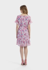 Blumenmusterkleid mit kurzen Rüschenärmeln, hellblauem Grund, rosa und lila Blumen, tailliert mit einem Gürtel und einem Rüschensaum. Rosa High-Heels.