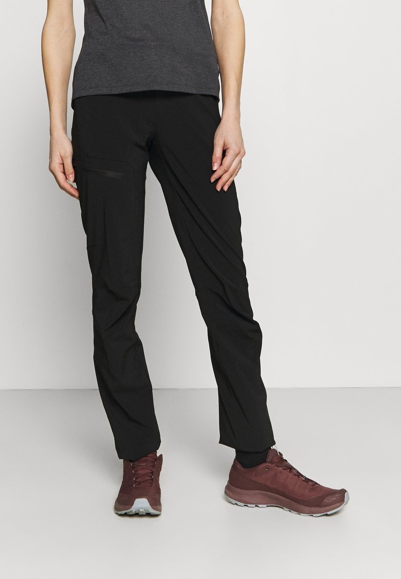 Sorte letvægtsbukser med slim fit, der har en lynlåslomme, kombineret med mørkerøde atletiksko. Glat tekstur og minimalistisk design.