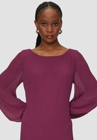 Robe prune à manches longues en tissu texturé. Elle présente une encolure bateau et des manches bouffantes transparentes, alliant élégance et confort.