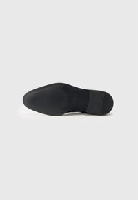 Suela de zapato negra con goma texturizada para mayor agarre. Presenta un ligero arco y puntera redondeada. Acabado suave con un pequeño tacón.