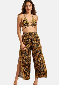 Un haut de bikini et un pantalon palazzo en tissu noir avec un motif floral doré. Le haut présente des bretelles fines, tandis que le pantalon a des fentes sur les côtés et une taille élastique.