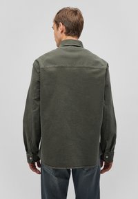 Dunkelgrünes Denim-Hemd mit Kragen, langen Ärmeln und Knopfmanschetten. Mit sichtbaren Nähten und einem lockeren Schnitt, von hinten gezeigt.