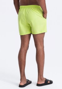 Vihreät uimahousut, joissa on joustava vyötärö ja sivutaskut, valmistettu kevyestä, nopeasti kuivuvasta materiaalista.