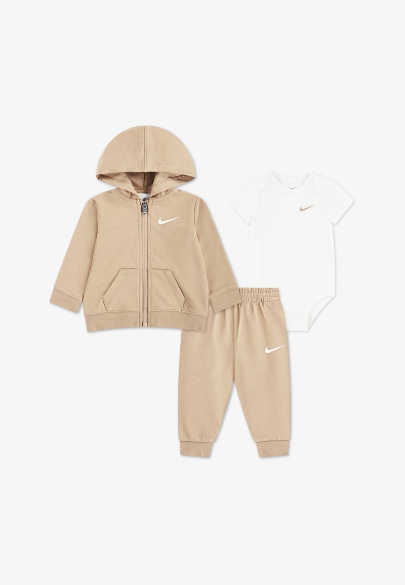 Felpa con zip beige con tasche frontali, pantaloni della tuta beige coordinati e body bianco a maniche corte, tutti con il logo Nike.