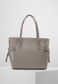 Sac fourre-tout en cuir gris avec deux longues poignées, une forme structurée et des accents en métal argenté. Présente une texture subtile et un détail de frange sur le côté.