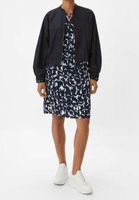 Bombers de la marina con puños acanalados sobre un vestido azul marino hasta la rodilla que presenta un patrón abstracto blanco. Completado con zapatillas blancas.