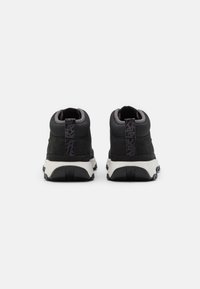 Černé tenisky s texturovaným povrchem, s vysokým designem, polstrovaným límcem a kontrastní bílou podešví. Zpevněná pata s poutkem.