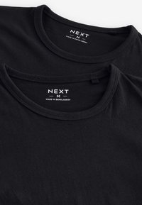 T-shirt neri in cotone impilati, con scollo rotondo e texture a costine, etichetta bianca con la scritta "NEXT M MADE IN BANGLADESH."