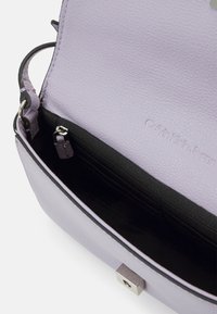 Světle fialová kabelka přes rameno z hrubé kůže s černým vnitřkem, vybavená rámovým uzávěrem a několika přihrádkami pro organizaci.