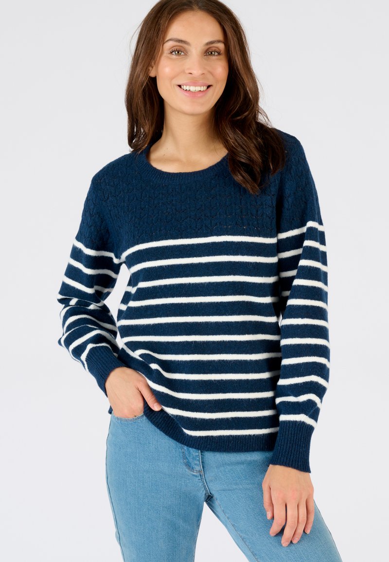 Suéter azul marino con rayas blancas, parte superior texturizada, cuello redondo y mangas largas, combinado con jeans azul claro.