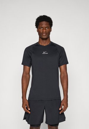 Man standing facing forward wearing a black Nike Pro short-sleeve shirt and black athletic shorts against a plain background.