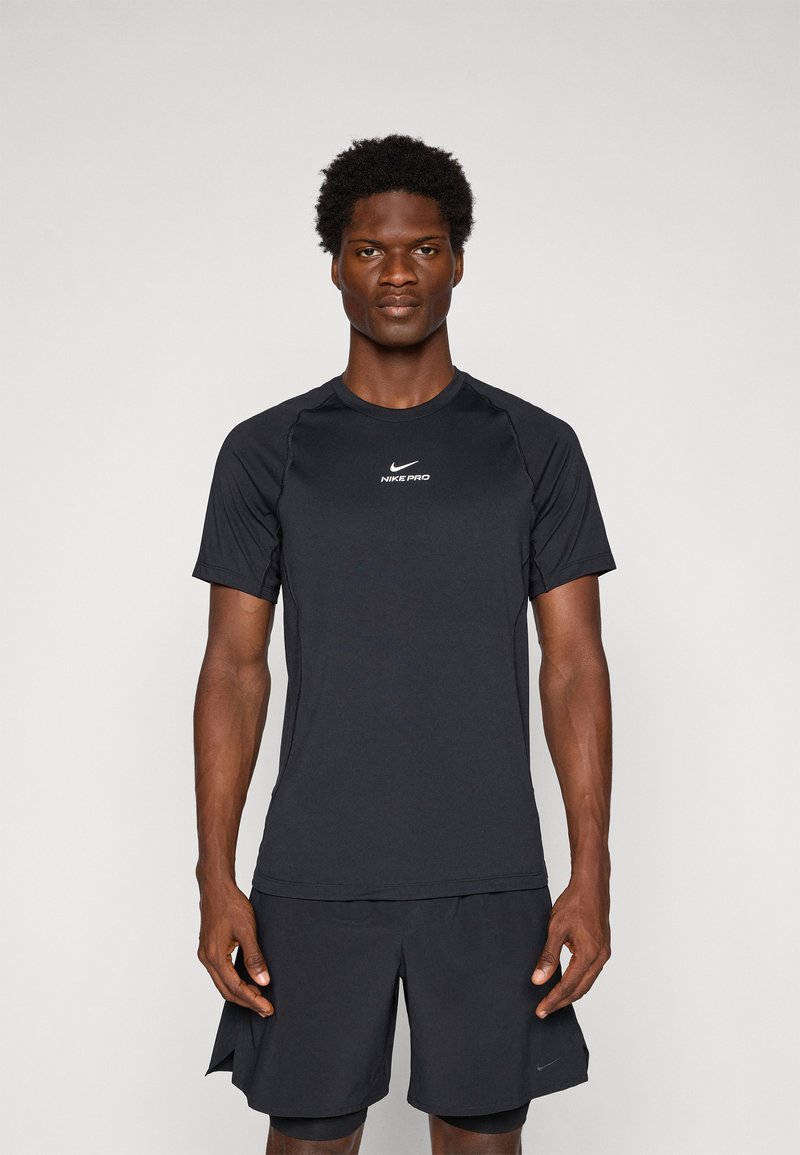 Mann som står vendt fremover iført en svart Nike Pro kortermet skjorte og svarte idrettsshorts mot en enkel bakgrunn.