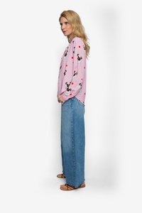 Roze blouse met lange mouwen en patronen van honden en harten; gecombineerd met wijde blauwe denim jeans en bruine sandalen met bandjes.