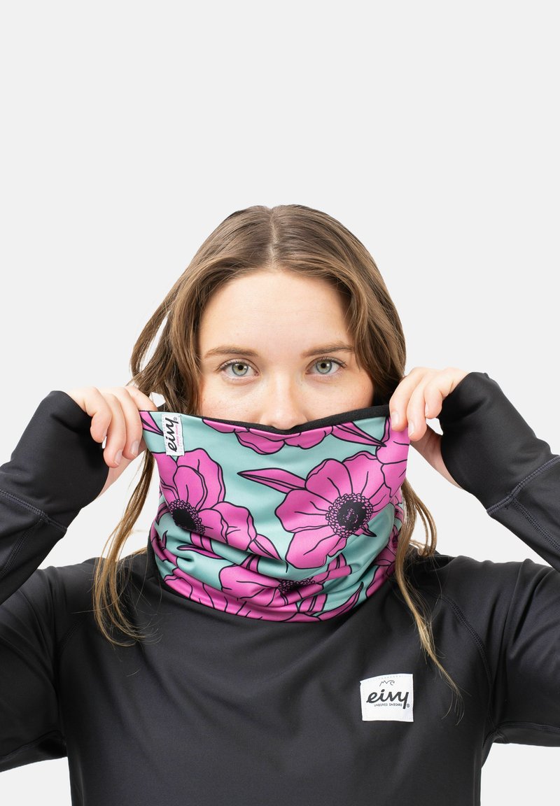 Bloemen halsdoek in turquoise met roze bloemen, gemaakt van zachte stof. Draagt door een persoon in een zwart shirt met lange mouwen met een logo.