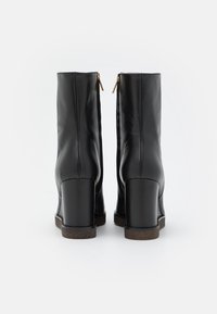 Botas negras de imitación cuero hasta el tobillo con un alto tacón cuadrado, cremalleras en la parte posterior y textura suave. La suela presenta un sutil patrón de relieve.