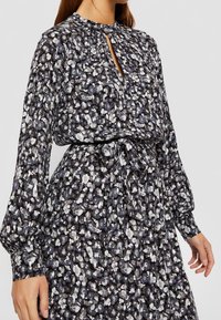 Blumenmuster-Kleid in Schwarz, Grau und Weiß, mit hohem Kragen, Schlüssellochöffnung, langen Ärmeln und einem Bindeband in der Taille. Leichter Stoff.