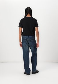 Svart crew-neck t-skjorte kombinert med løstsittende blå jeans med flere lommer og en falmet tekstur, båret med svarte sko.