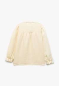 Langsleeve, crèmekleurige blouse van textuurstof. Heeft gathers op de schouders en gerimpelde manchetten. Eenvoudig, ontspannen ontwerp aan de achterkant met een yoke-detail.