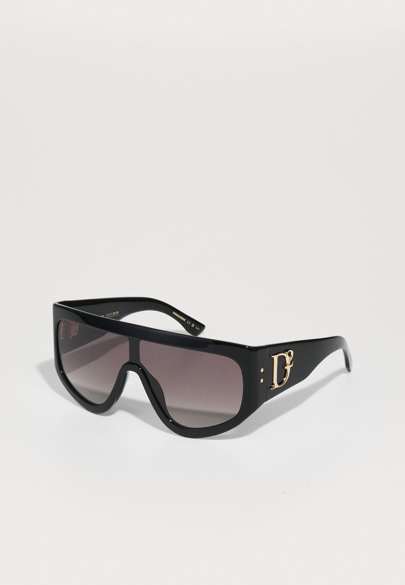 Black oversized sunglasses with gradient lenses, featuring a bold gold logo accent and smooth plastic frame. Angular shape with thick arms.