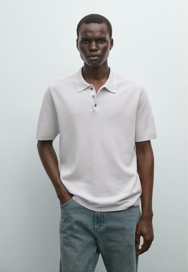 Polo a maniche corte di colore grigio chiaro con una finitura texturizzata e tre bottoni, abbinato a jeans denim blu larghi.