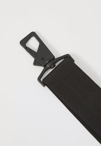 Fekete nylon öv texturált felülettel. Fekete fém csattal rendelkezik, négyzet alakú hurokkal a biztonságos rögzítés érdekében.
