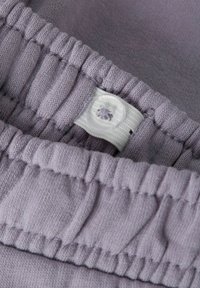 Miękka, lawendowa elastyczna tkanina z paskiem w talii o marszczonej fakturze. Wyposażona w biały, przypominający guzik zamek do pewnego zapięcia.