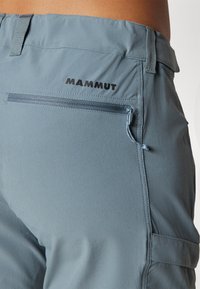 Šviesiai mėlynos žygio kelnės su užtrauktuku užpakalinėje kišenėje, plokščia juosmeniu ir lygiu paviršiumi. Juodas logotipas "MAMMUT".