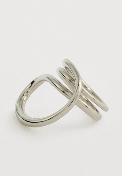 Λευκόχρυσο, διπλό δαχτυλίδι με λείες, καμπυλωτές ζώνες που επικαλύπτονται σε απλό φωτεινό φόντο.