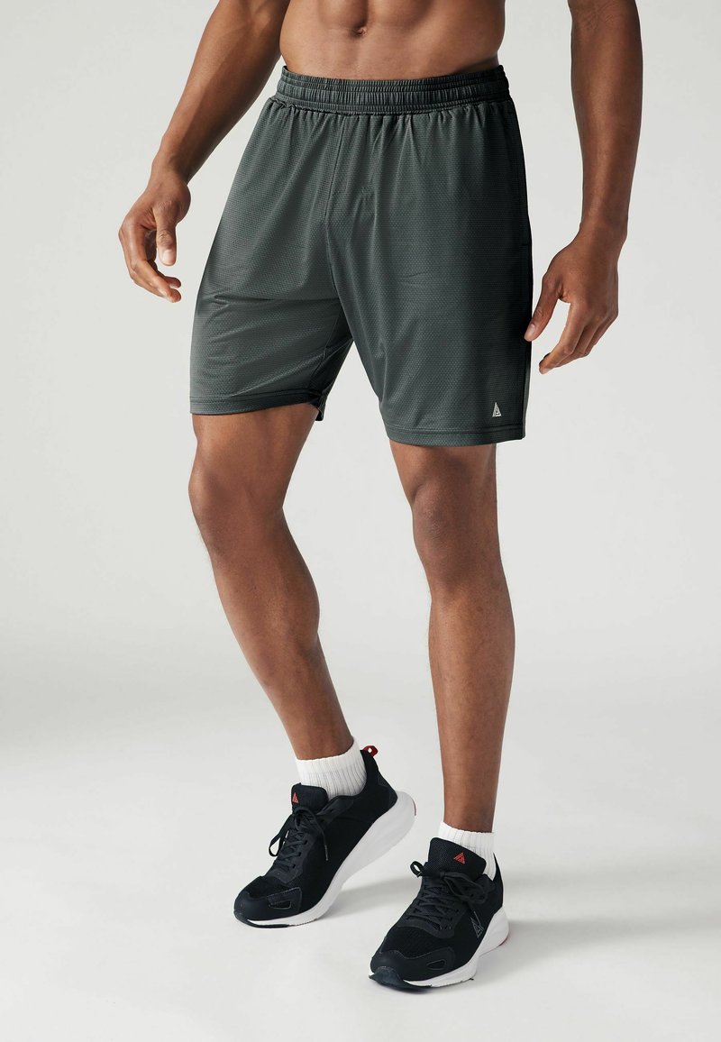 Mørkegrå træningsshorts med elastisk talje, let materiale og subtil tekstur. Parret med sorte sneakers og hvide sokker.