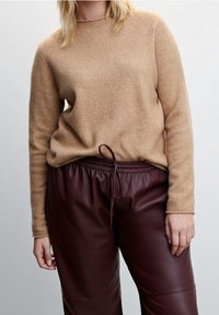 Beige cashmere sweater with a round neckline, paired with burgundy faux leather pants featuring an adjustable drawstring waist.