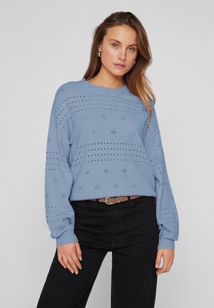 Hellblaues gestricktes Sweatshirt mit Punktmuster und überschnittenen Schultern, kombiniert mit schwarzen Hosen und einem Gürtel. Weicher Stoff mit gerippten Bündchen.