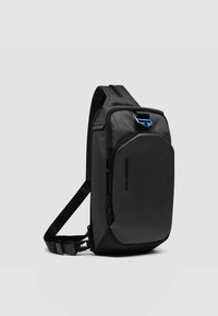 Bolso bandolera de nylon negro con acabado texturizado, que cuenta con un gran bolsillo frontal, correa ajustable y herrajes con acento azul.