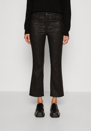 Pantalons flare noirs courts avec un subtil motif peau de serpent, portés avec des mocassins noirs et un haut à manches longues noir.