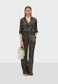 Black sheer blouse with a polka dot pattern, paired with fitted black pants featuring similar dots. Accessorized with a white handbag.