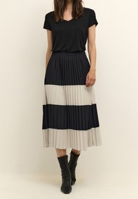 Černá plisovaná sukně s převládajícími tmavě modrými a světle béžovými vodorovnými pruhy; elastický pas; kombinovaná s černým krátkým tričkem a černými botami.