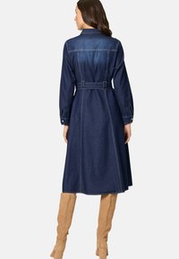 Denim jurk met lange mouwen, een ceintuur in de taille en een getailleerd lijfje. Donkerblauwe kleur met contrasterende stikdetails. Lengte tot halverwege de kuiten.