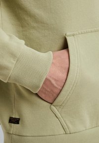 Felpa verde chiaro con polsini a coste, dotata di una tasca laterale. Tessuto a trama e un piccolo etichetta tessuta sull'orlo.