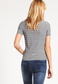 Camiseta de manga corta a rayas en gris y blanco, hecha de material suave. Presenta un corte ajustado y llega hasta la cintura, combinada con jeans azules.