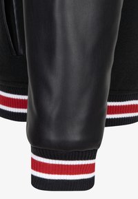 Manche en cuir noir avec un corps en laine, présentant des poignets à côtes avec des rayures noires, rouges et blanches. Texture lisse et style athlétique.