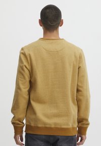 Sudadera amarilla de manga larga, con cuello redondo y puños acanalados. Textura suave con un acabado jaspeado y una cinturilla ligeramente elástica.