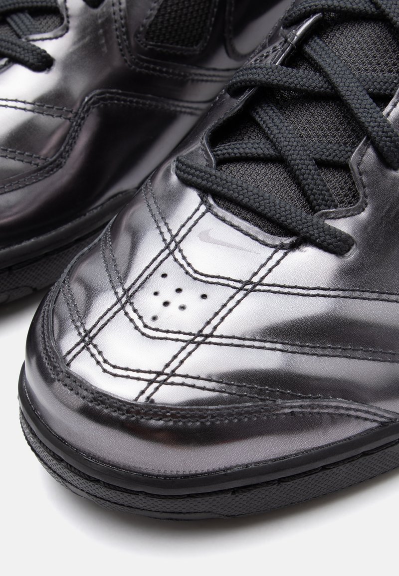 Schwarze synthetische Sneakers mit glänzender Oberfläche, strukturierten Mesh-Einsätzen, gepolsterter Zunge und traditioneller Schnürung. Verfügt über perforierte Details.