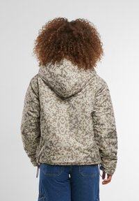 Reversējams pūkains mētelis bēšā kamuflāžas rakstā, ar kapuci, auklas apakšmalu un elastīgām aprocēm papildu siltumam.