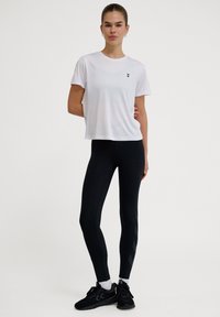 Vit träningströja med korta ärmar och svart logga; svarta leggings med texturerade sidodelar; svarta träningsskor med snörning.