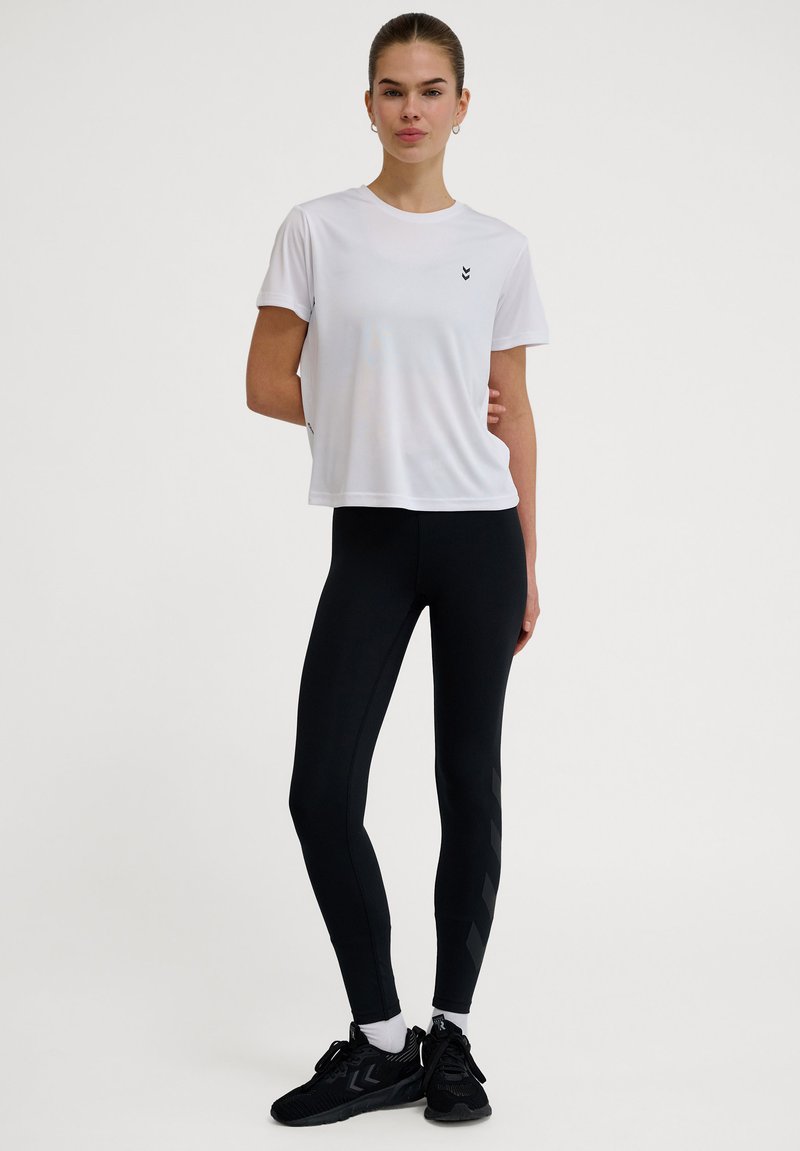 Vit träningströja med korta ärmar och svart logga; svarta leggings med texturerade sidodelar; svarta träningsskor med snörning.